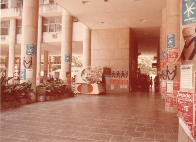 Na entrada da Ala Frings, paredes cobertas com propagandas do movimento estudantil na PUC-Rio. Ao centro a banca de jornal que ficava onde atualmente há um caixa eletrônico. 1985. Fotógrafo desconhecido. Acervo do Projeto Comunicar. Na entrada da Ala Frings, paredes cobertas com propagandas do movimento estudantil na PUC-Rio. Ao centro a banca de jornal que ficava onde atualmente há um caixa eletrônico. 1985. Fotógrafo desconhecido. Acervo do Projeto Comunicar.